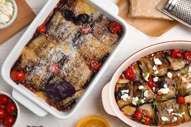 Tasty eggplant rolls in baking dishes on white wooden table, flat lay