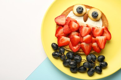 Creative serving for kids. Plate with cute owl made of pancakes, berries, cream, banana and almond on color background, top view. Space for text