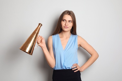 Young woman with megaphone on light background