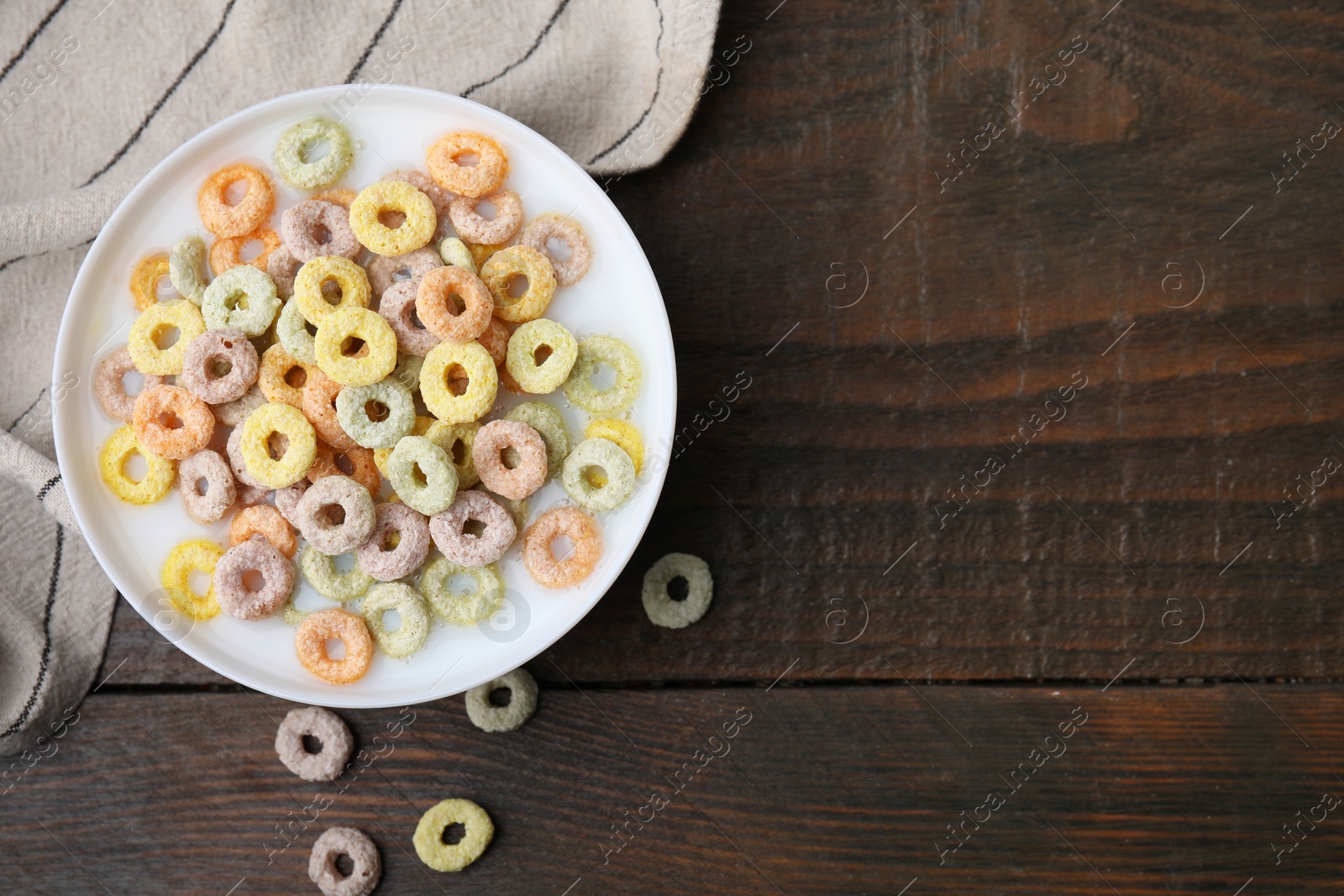 Photo of Cereal rings and milk in bowl on wooden table, top view. Space for text