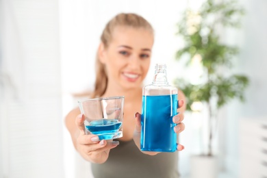 Photo of Woman holding bottle and glass with mouthwash in bathroom. Teeth care