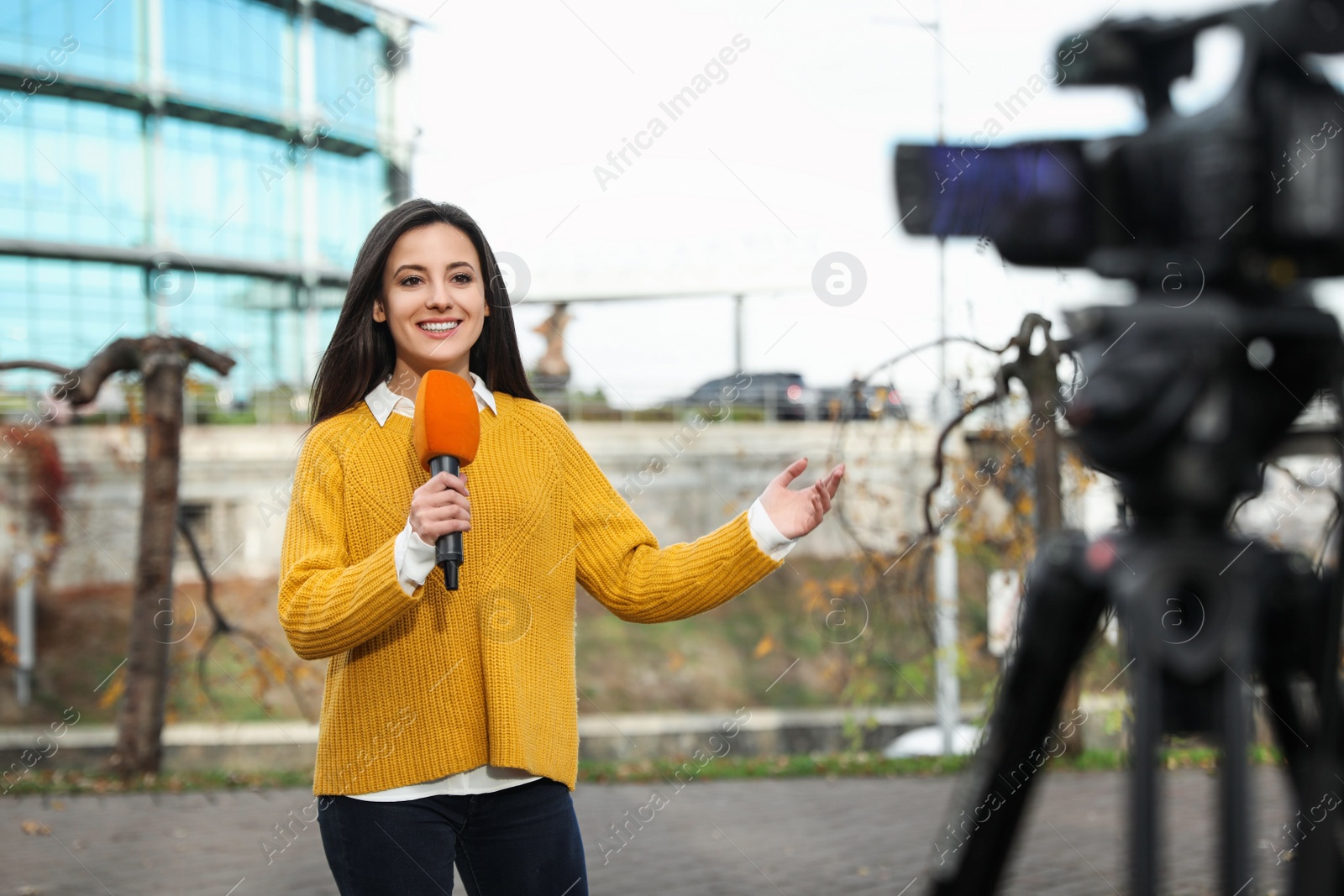 Photo of Young female journalist with microphone working on city street