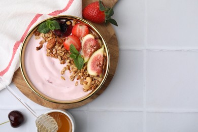 Photo of Bowl with yogurt, fruits, granola and honey on white tiled table, flat lay. Space for text