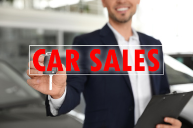 Salesman with key and clipboard in car dealership, closeup