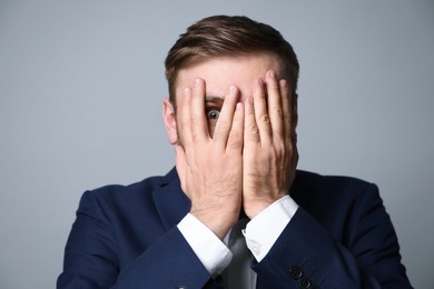 Young businessman feeling fear on grey background