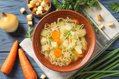 Photo of Bowl of fresh homemade vegetable soup with ingredients on blue wooden table, flat lay