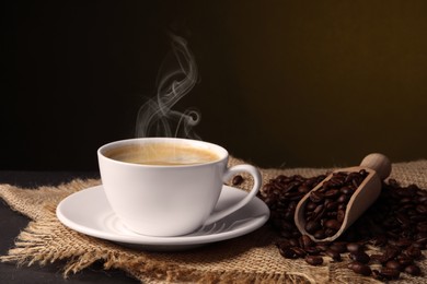 Image of Steaming coffee in cup and roasted beans on table