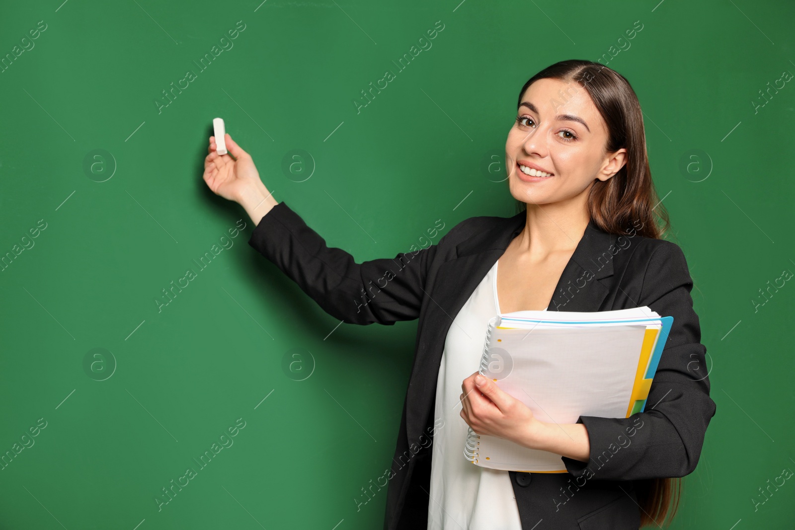 Photo of Portrait of young teacher with notebook and chalk on green background. Space for text