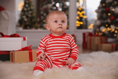 Cute baby in bright Christmas pajamas on floor at home