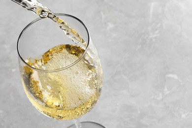 Photo of Pouring tasty aromatic wine in glass at gray marble table, closeup. Space for text