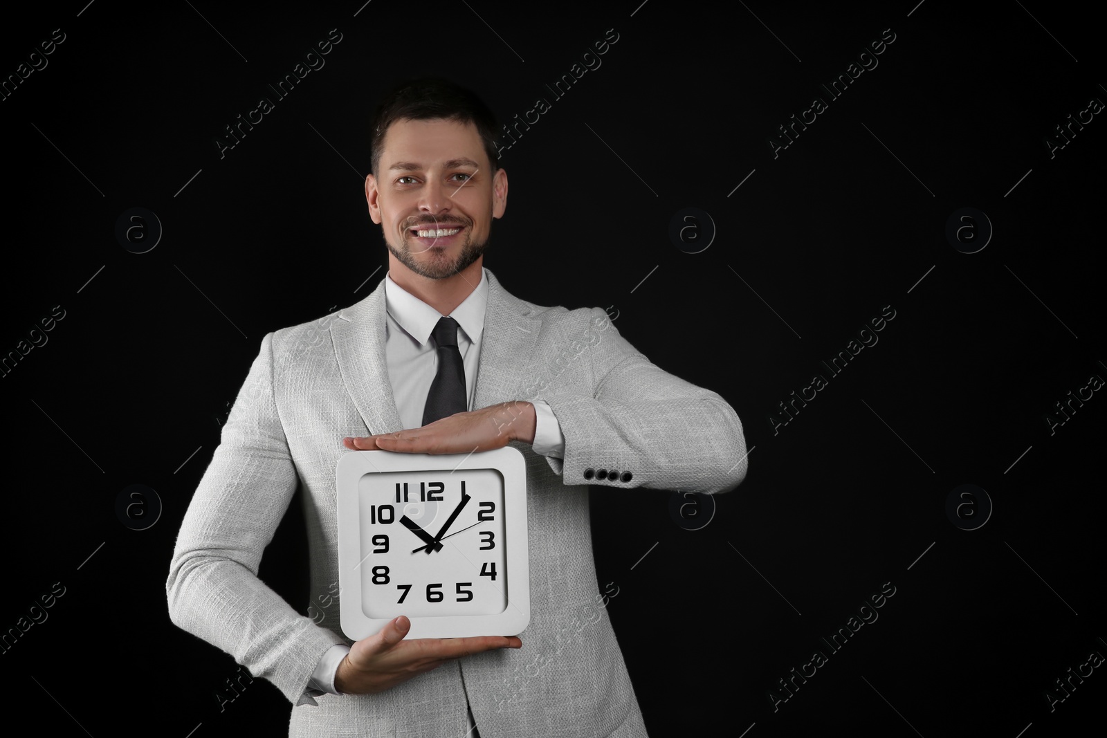 Photo of Happy businessman holding clock on black background, space for text. Time management