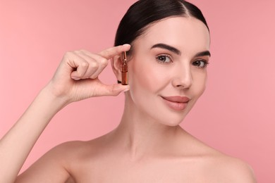 Photo of Beautiful young woman holding skincare ampoule on pink background