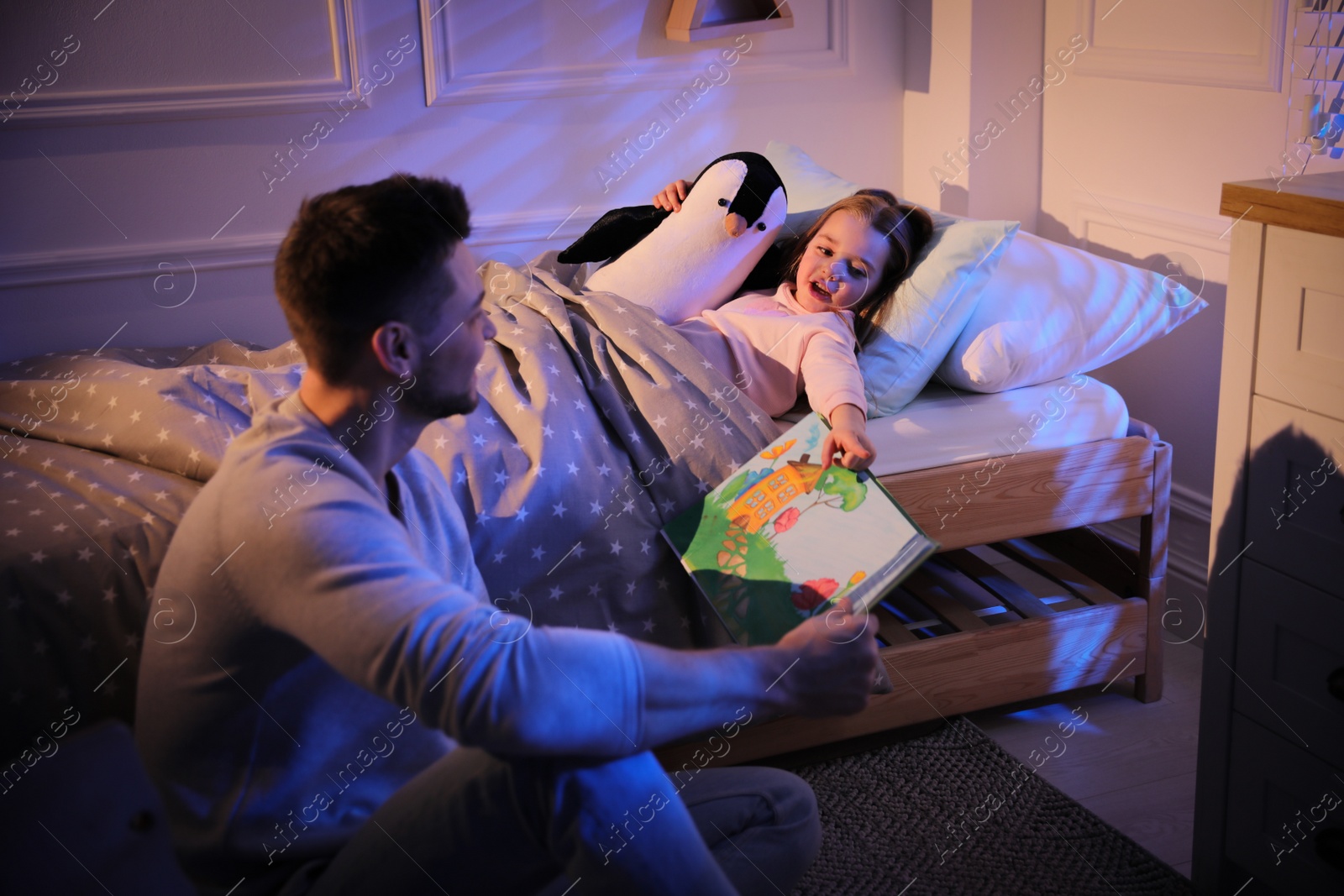 Photo of Father reading bedtime story to his daughter at home