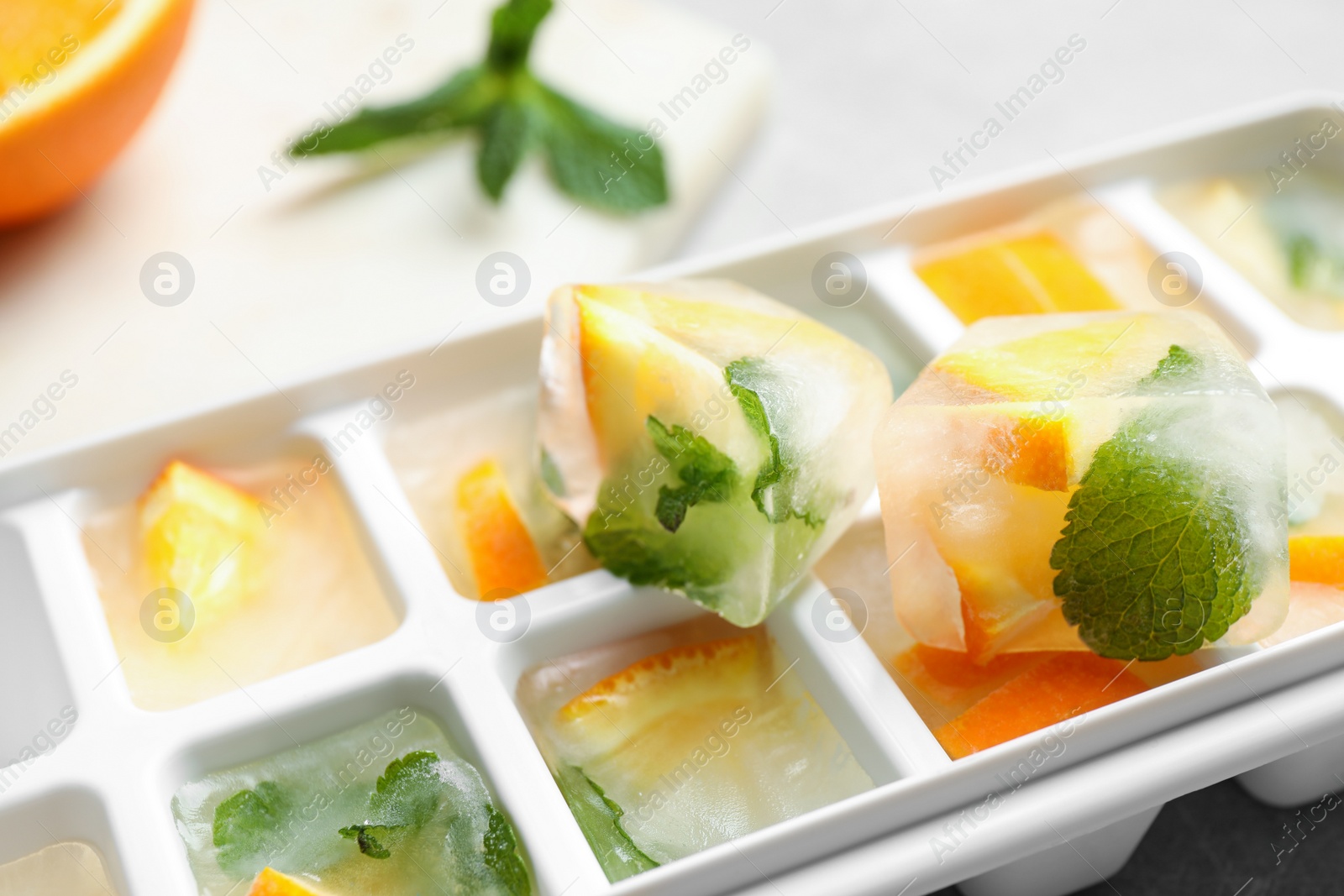 Photo of Ice cubes with orange and mint on light table, closeup