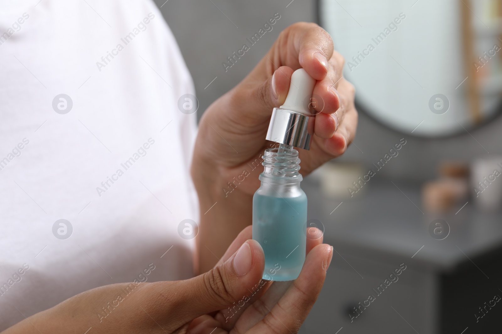 Photo of Woman with bottle of cosmetic serum and dropper indoors, closeup