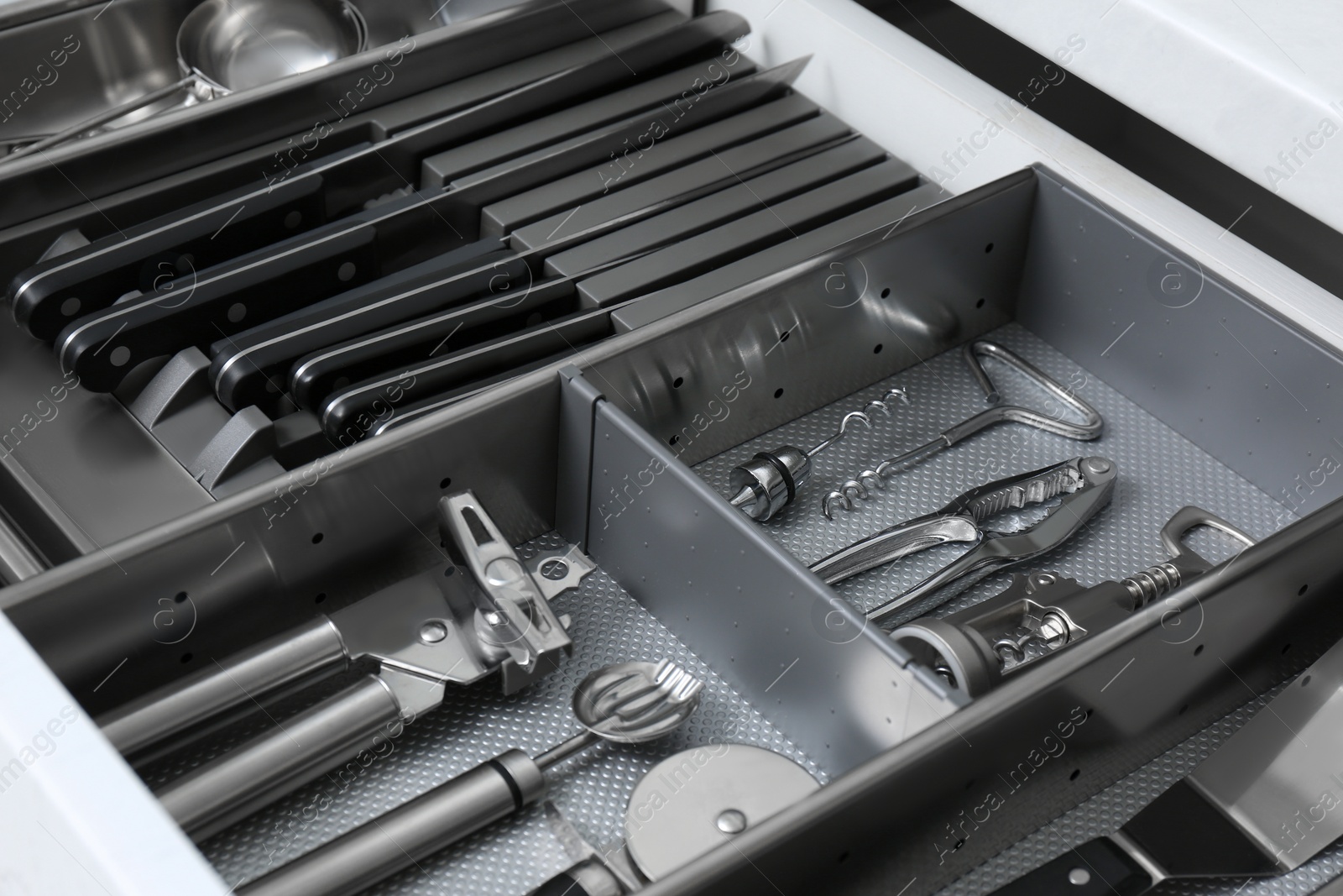 Photo of Open drawer with stainless steel utensil set, closeup. Order in kitchen