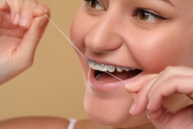 Woman with braces cleaning teeth using dental floss on brown background, closeup