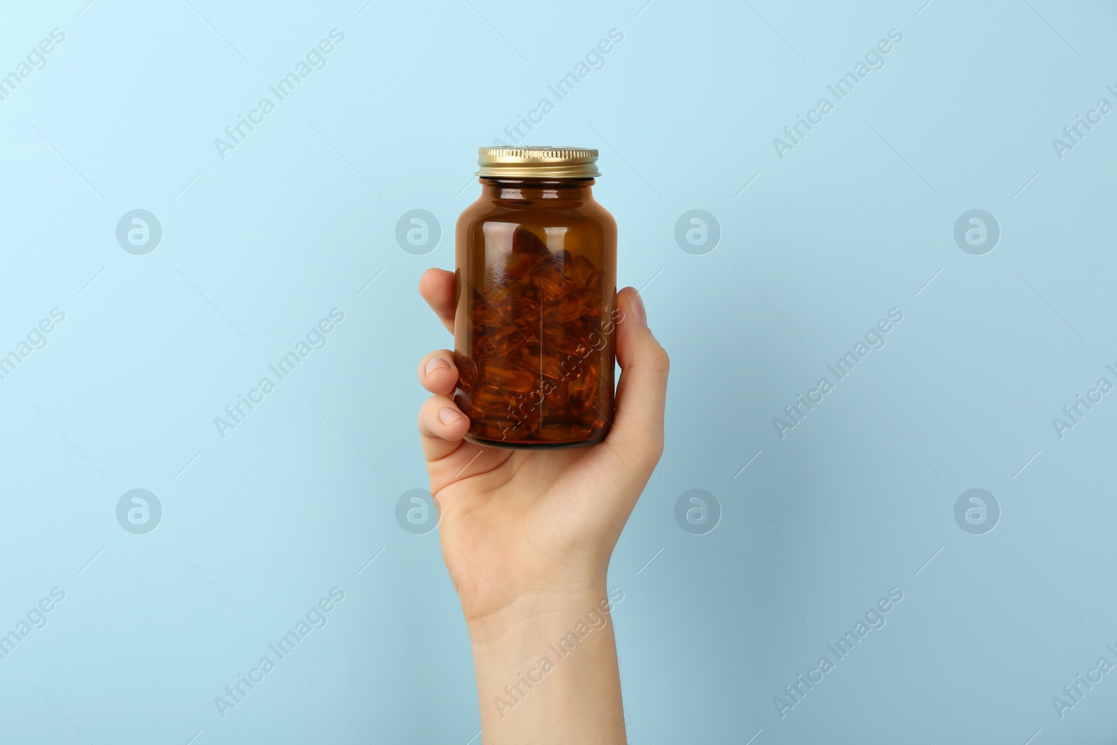 Photo of Woman holding jar with vitamin capsules on light blue background, closeup