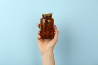 Photo of Woman holding jar with vitamin capsules on light blue background, closeup