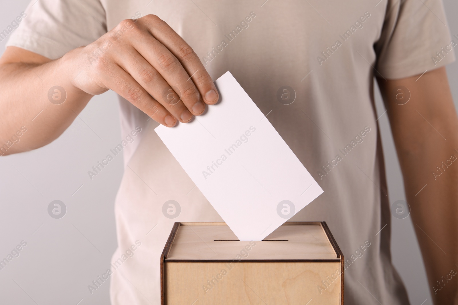 Photo of Man putting his vote into ballot box on light grey background, closeup