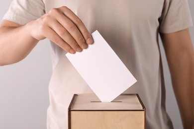 Photo of Man putting his vote into ballot box on light grey background, closeup