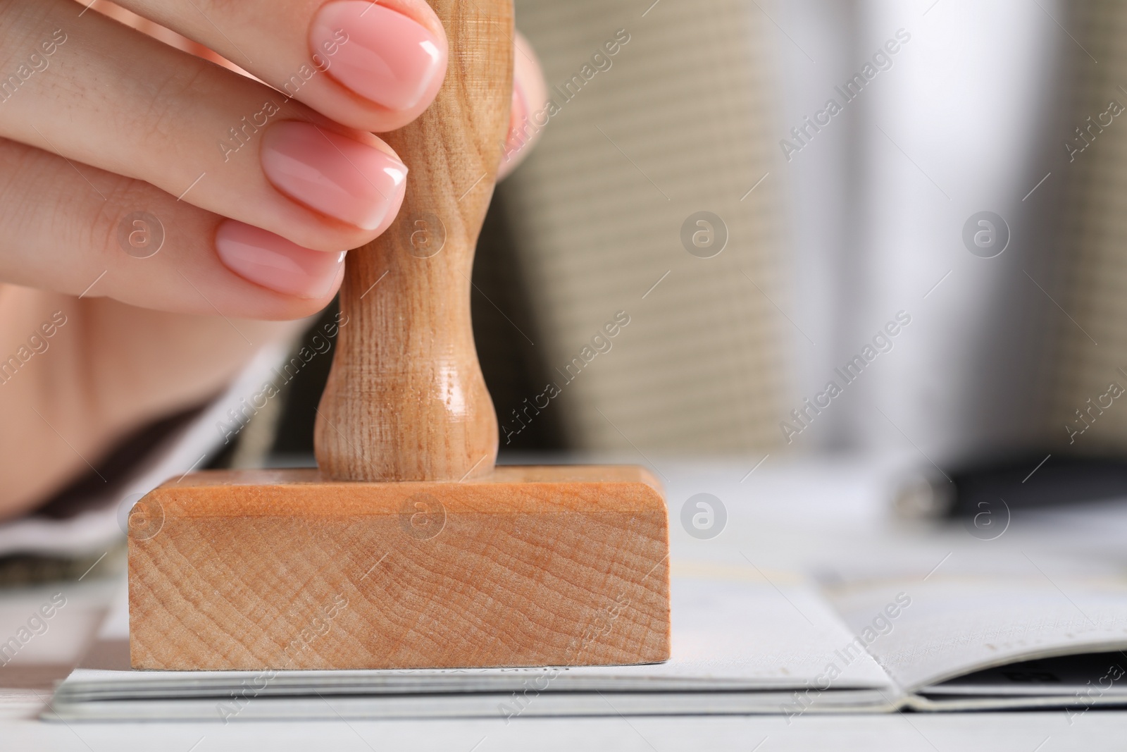 Photo of Ukraine, Lviv - September 6, 2022: Woman stamping visa page in passport at white wooden table, closeup