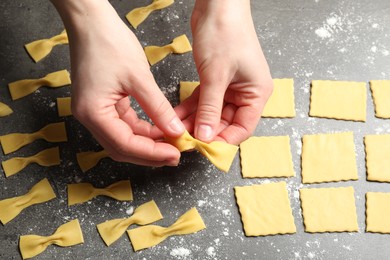 Woman making farfalle pasta at grey table, closeup