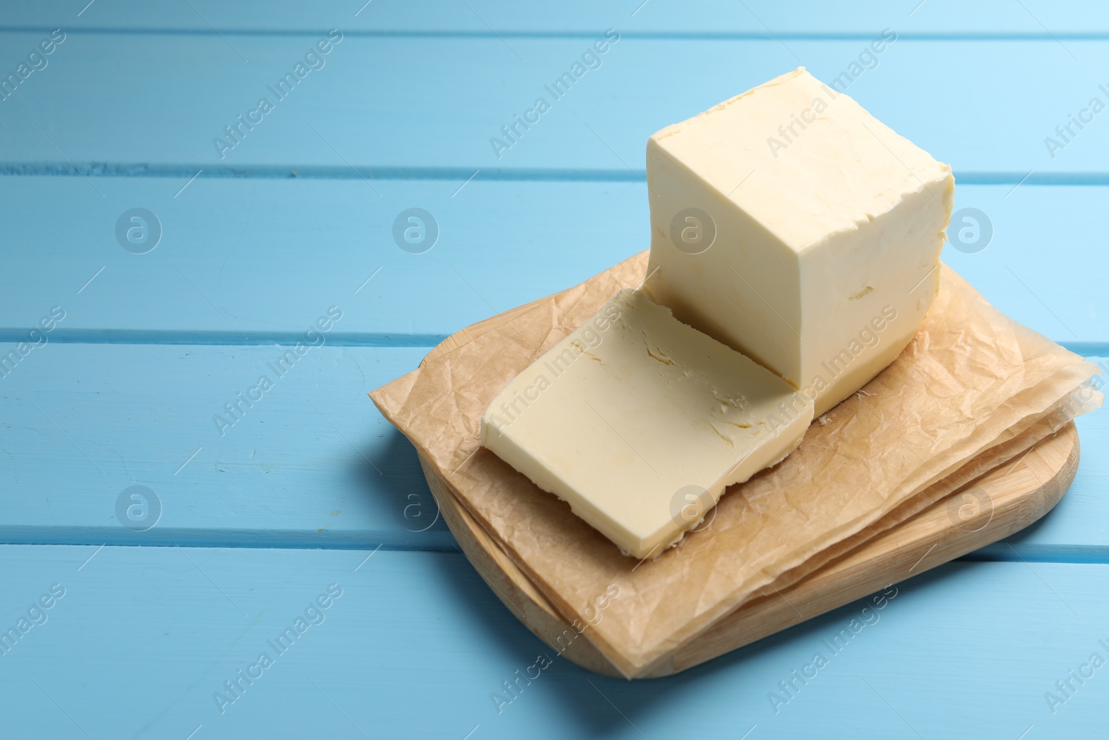 Photo of Block of tasty butter on light blue wooden table. Space for text