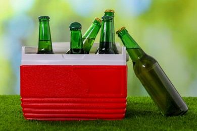 Plastic cool box with glasses of drink on artificial grass, closeup