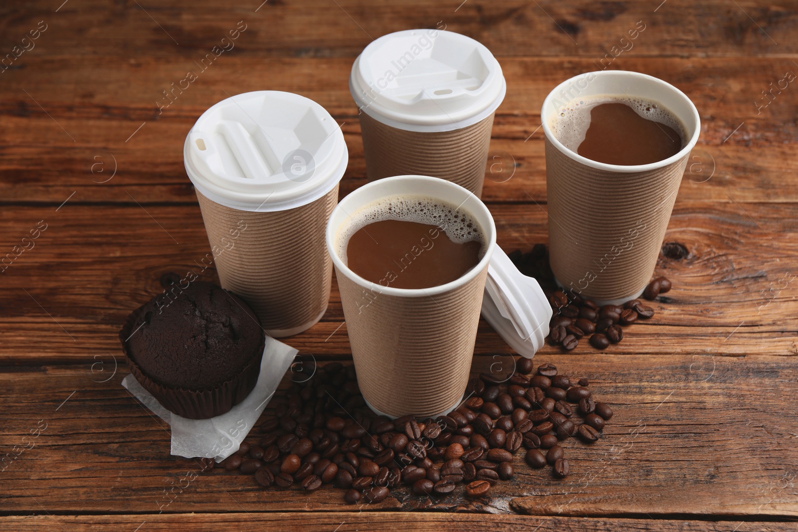 Photo of Coffee to go. Paper cups with tasty drink, muffin and beans on wooden table