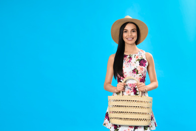 Young woman wearing floral print dress with straw bag on light blue background. Space for text