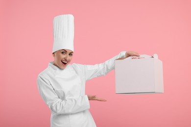 Photo of Happy professional confectioner in uniform showing cake box on pink background