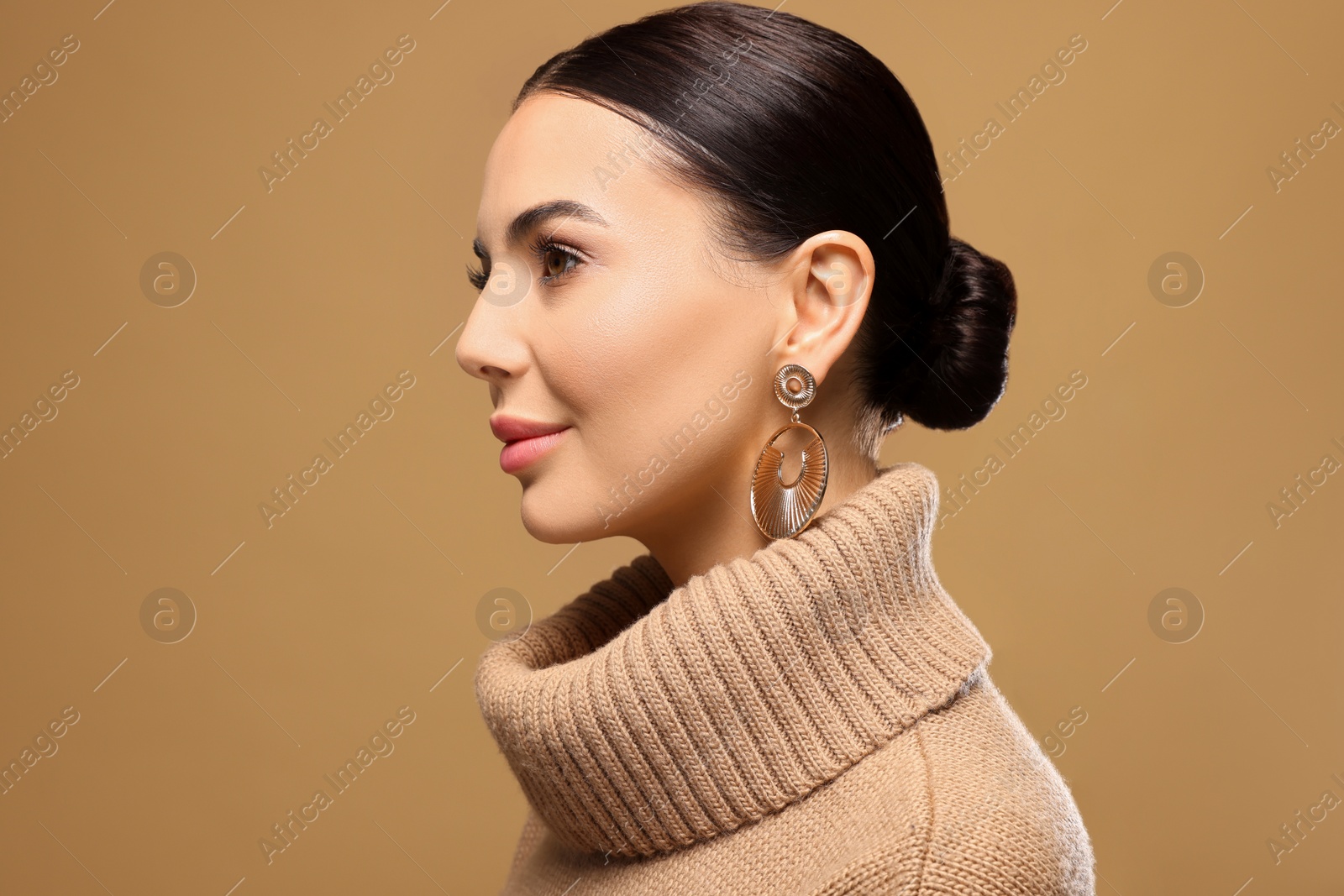 Photo of Beautiful young woman with elegant earrings on light brown background