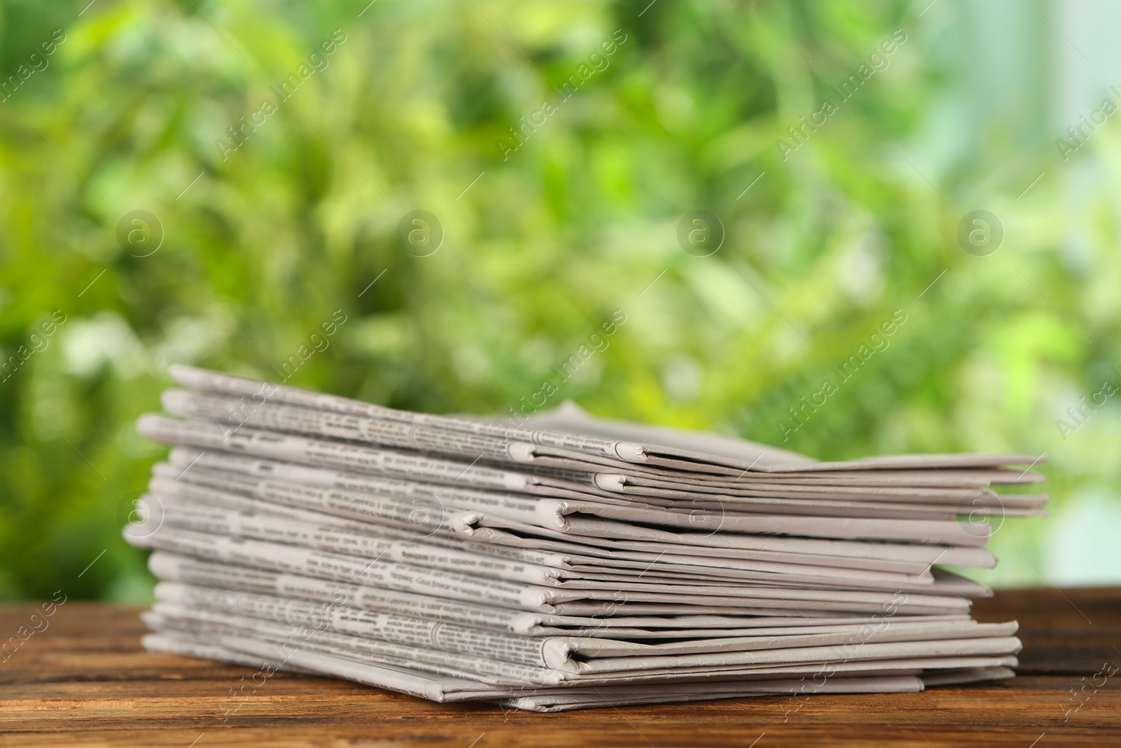 Photo of Stack of newspapers on wooden table against blurred green background. Journalist's work