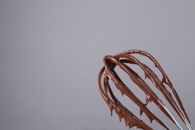 Whisk with chocolate cream on grey background, closeup. Space for text