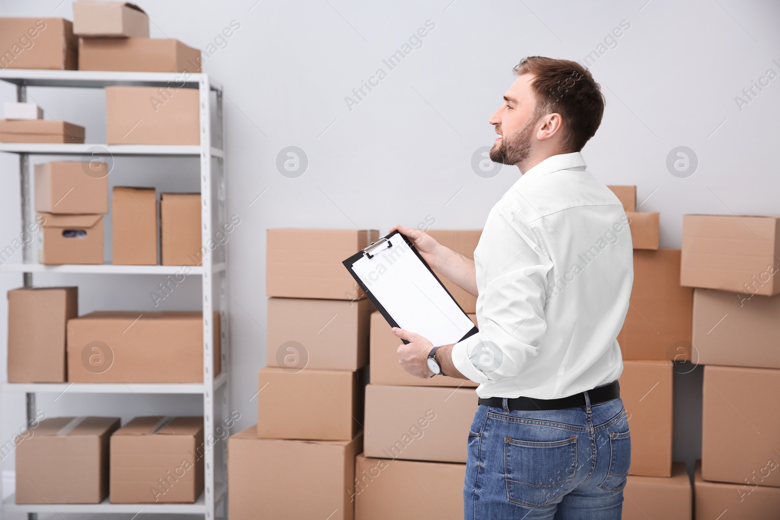 Photo of Young businessman with clipboard near cardboard boxes at warehouse