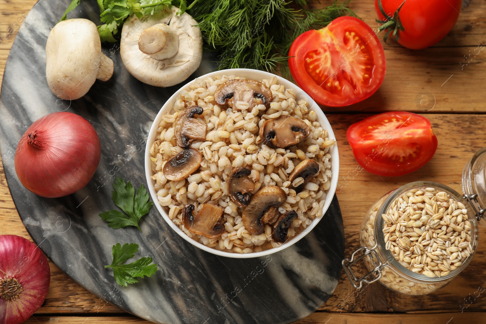 Photo of Delicious pearl barley in bowl served on wooden table, flat lay