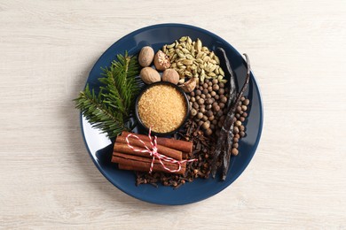 Plate with different aromatic spices and fir branches on light wooden table, top view