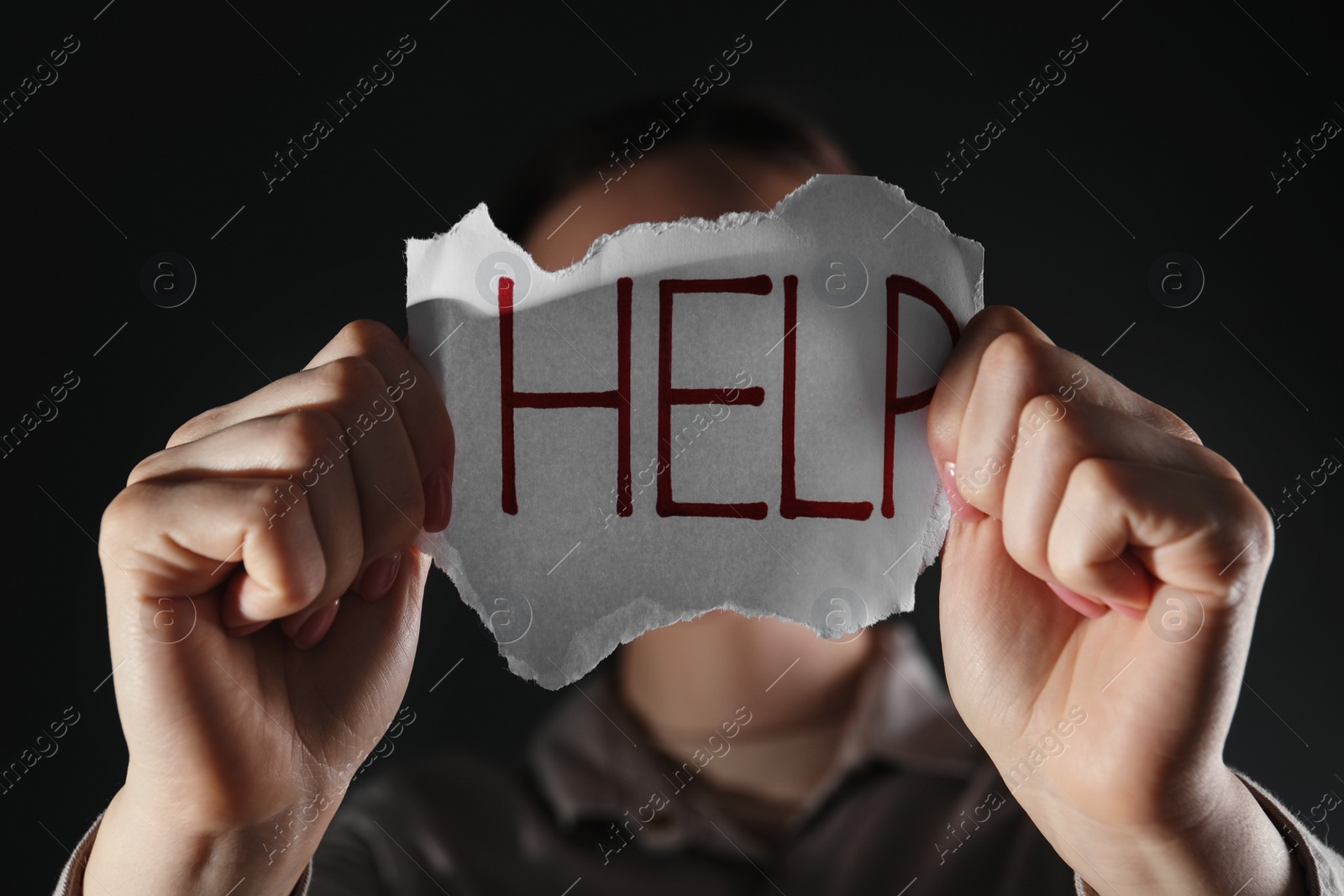 Photo of Woman holding piece of paper with word Help on black background, closeup. Domestic violence concept