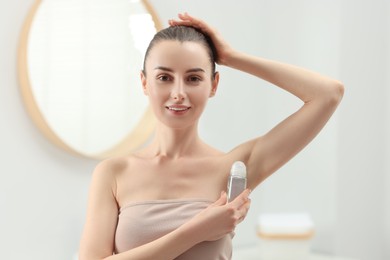 Photo of Beautiful young woman applying deodorant in bathroom