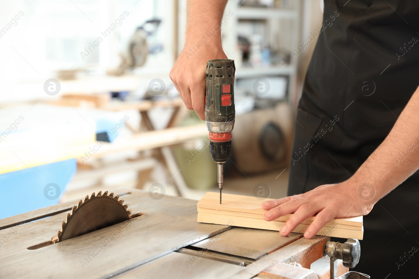 Photo of Working man using electric screwdriver at carpentry shop, closeup. Space for text