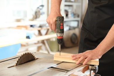 Working man using electric screwdriver at carpentry shop, closeup. Space for text