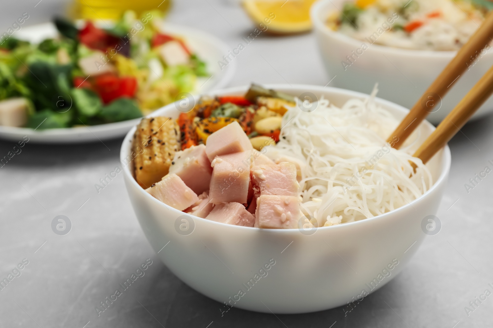 Photo of Tasty cooked rice noodles with chicken and vegetables on grey marble table