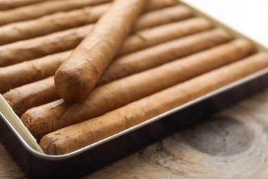 Photo of Many expensive cigars in box on wooden table, closeup