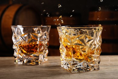 Photo of Glasses with whiskey on table against wooden barrels, closeup