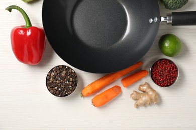 Empty iron wok surrounded by raw ingredients on white wooden table, flat lay