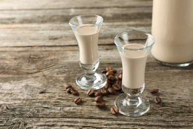 Photo of Coffee cream liqueur in glasses and beans on wooden table, space for text