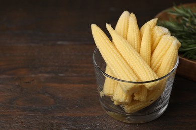 Photo of Tasty fresh yellow baby corns in glass on wooden table, space for text