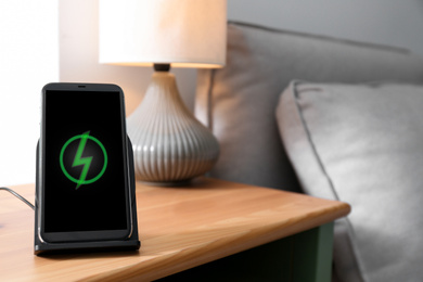 Photo of Smartphone charging on wireless pad in room. Space for text