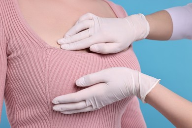Mammologist checking woman's breast on light blue background, closeup
